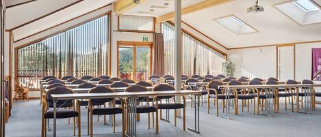 A conference room with long tables and chairs, large windows, and a high ceiling with skylights.