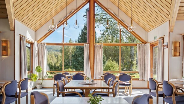 A dining area with large windows, wooden ceiling, and blue chairs. - Heia Gjestegård (Grong)