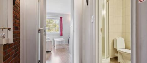 A hotel bathroom with a shower, toilet, and a window with a pink curtain.