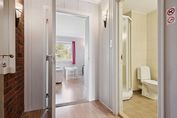 Un baño de hotel con ducha, inodoro y ventana con cortina rosa.