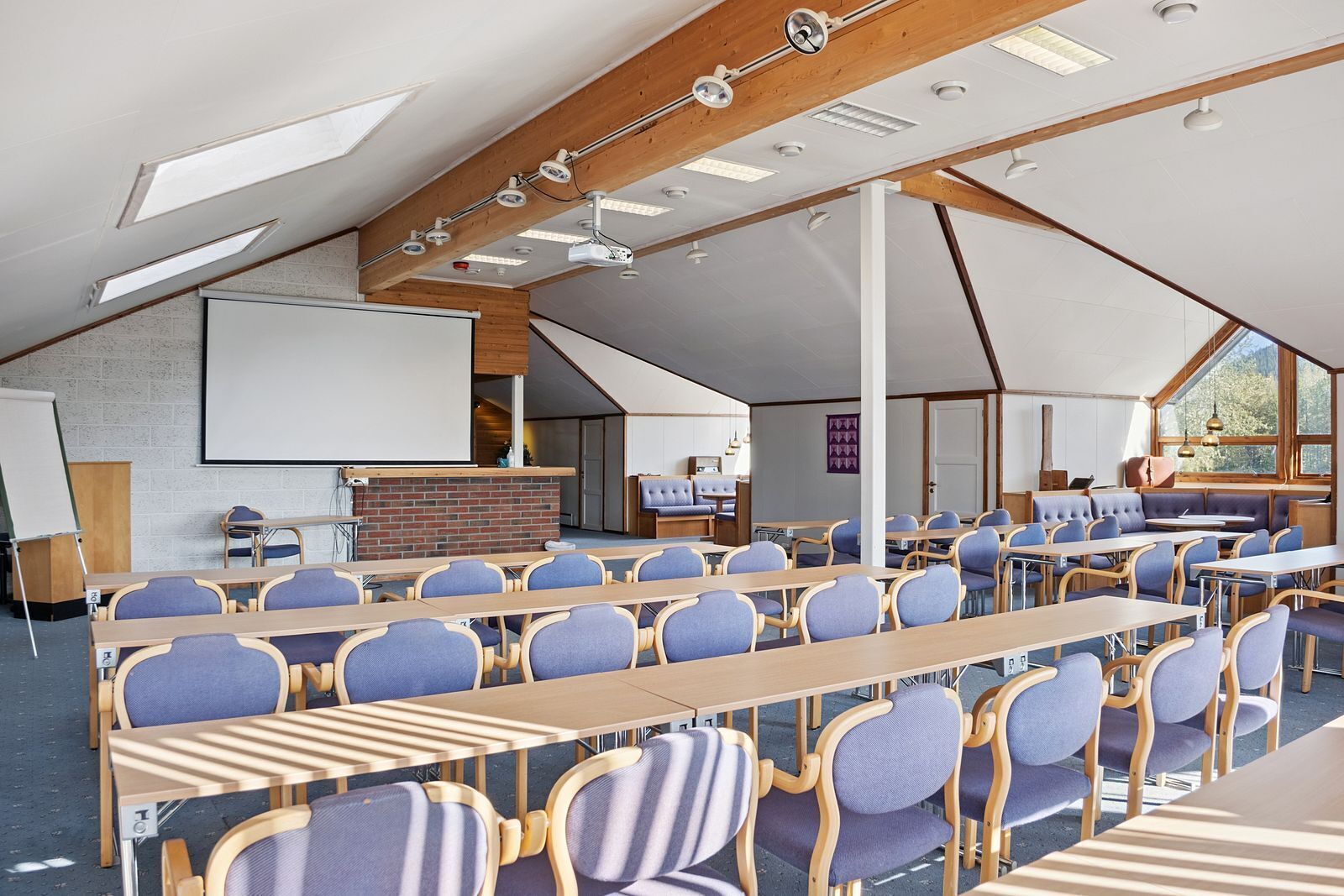 A conference room with long tables, chairs, a whiteboard, and a stage area.