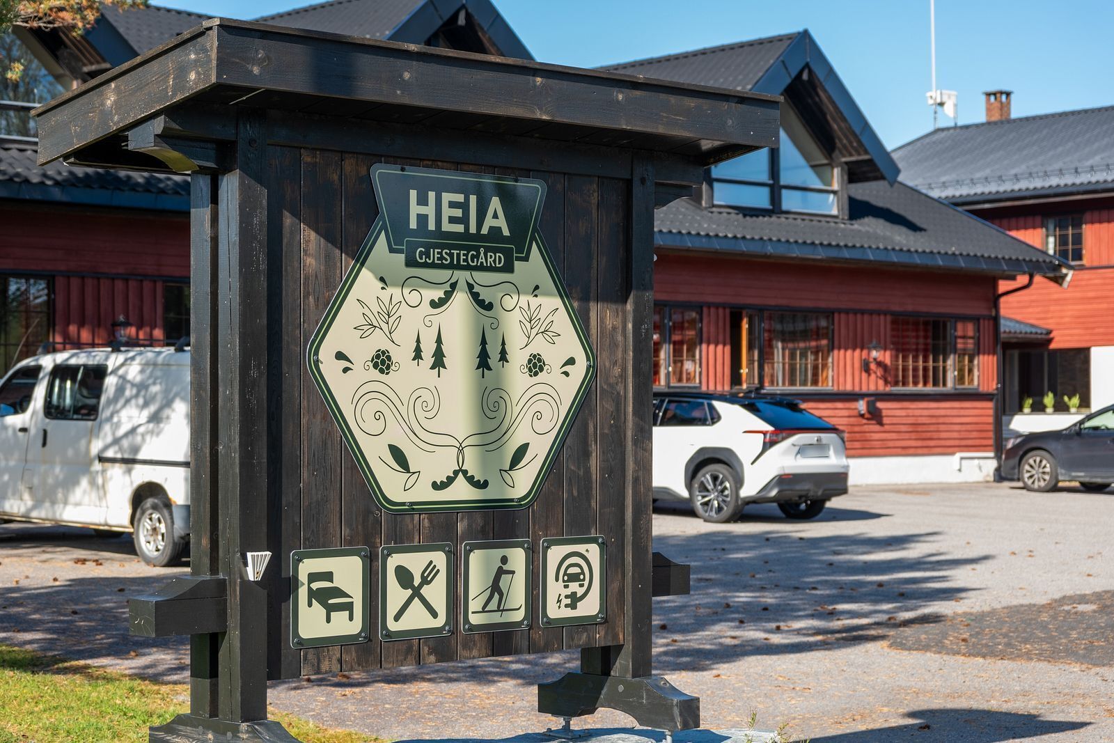 Un panneau en bois indiquant « HEIA GJESTEGÅRD » et comportant des symboles pour le stationnement, la restauration et la randonnée.