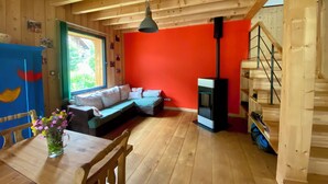 A wooden interior with a red wall, a sofa, a table with a vase of flowers, a hanging light fixture, and a staircase. - Hideaway at the foot of Mont Blanc (Les Houches)