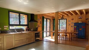 A modern kitchen with wooden cabinets, a large window, and a dining area with wooden tables and chairs. - Hideaway at the foot of Mont Blanc (Les Houches)