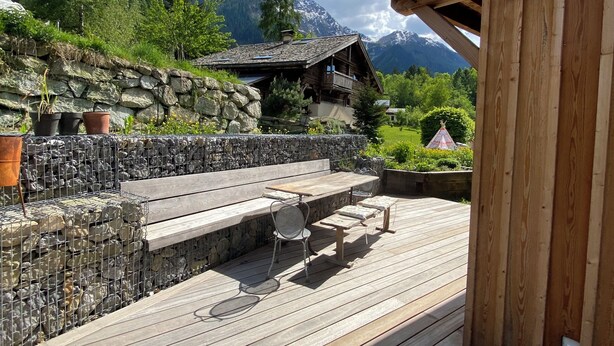 A wooden deck with outdoor seating, a stone wall, and a mountain backdrop. - Hideaway at the foot of Mont Blanc (Les Houches)