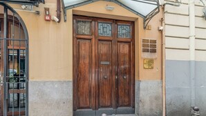 Puerta doble de madera con una pequeña ventana arriba, una reja metálica a la izquierda y un escalón de hormigón que lleva a la puerta.