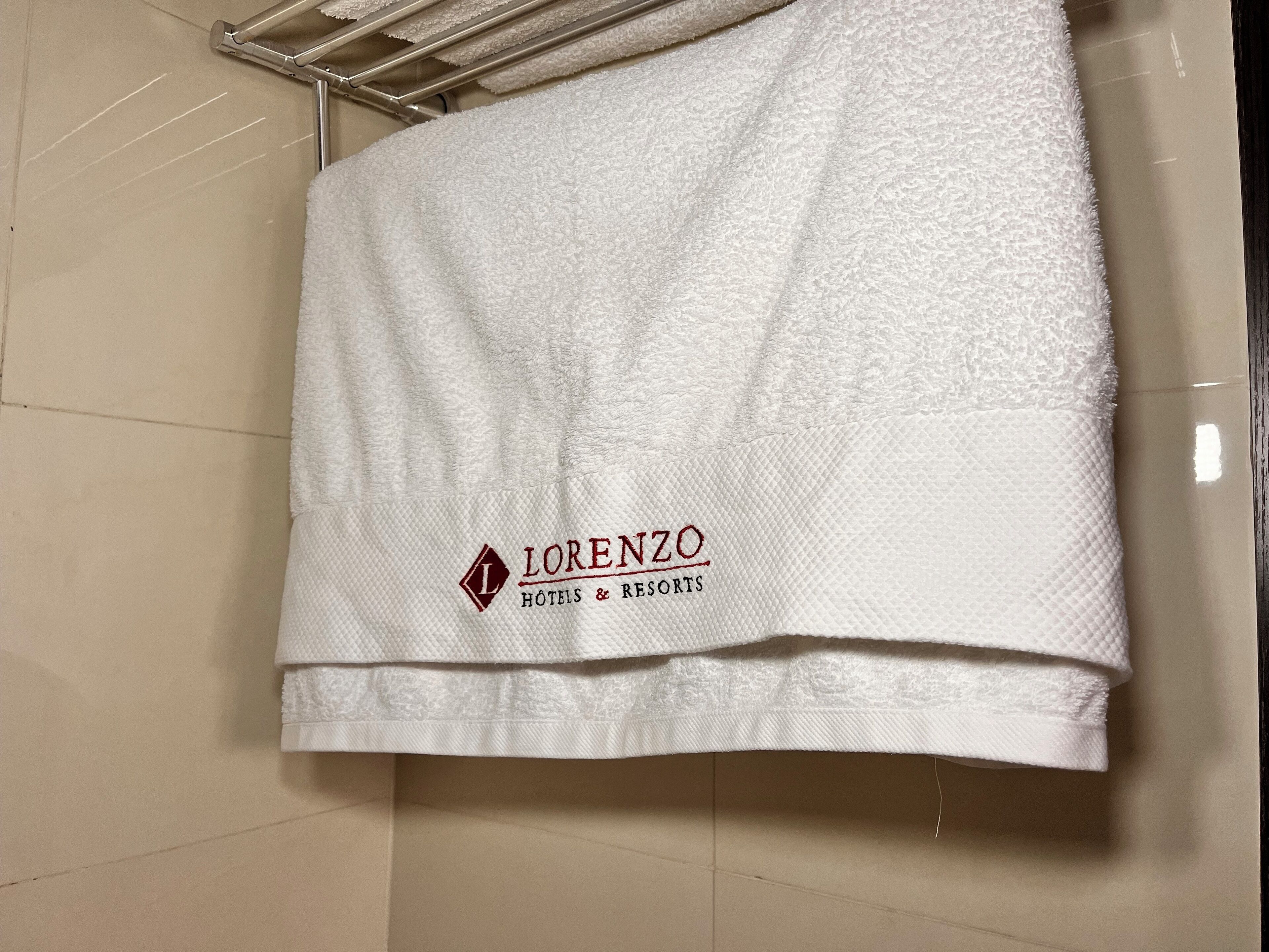 A white towel hanging on a metal rack with the logo 'Lorenzo Hotels & Resorts' on it.