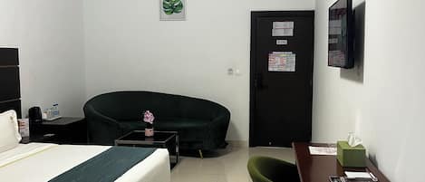 Ein Hotelzimmer mit einem Bett, einem Schreibtisch, einem Sessel, einer Couch, einem kleinen Tisch mit Blumen und einer Tür mit Sicherheitshinweis.