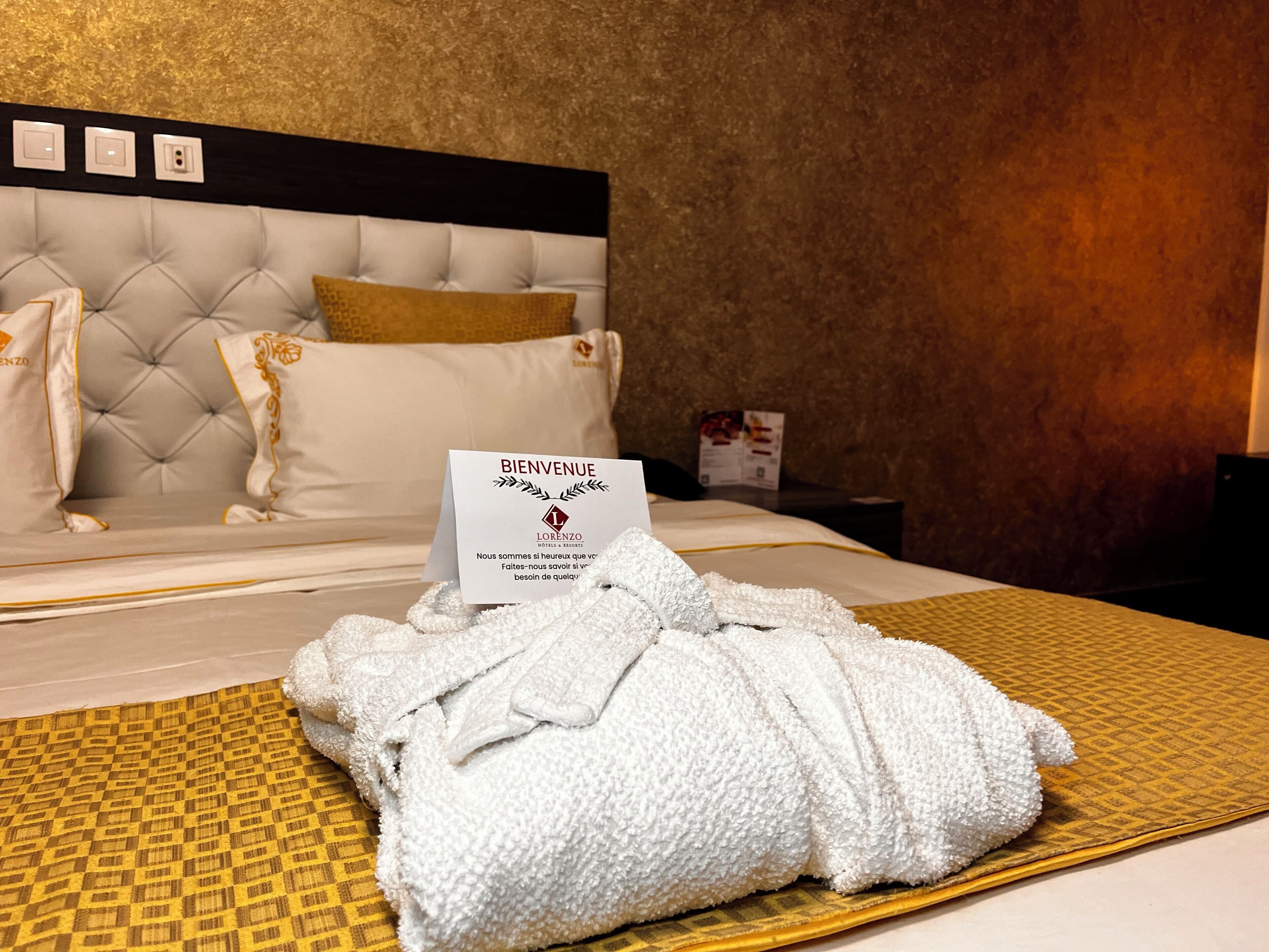 Habitació d'hotel amb un llit ben fet, un cartell de benvinguda i una tovallola al llit.
