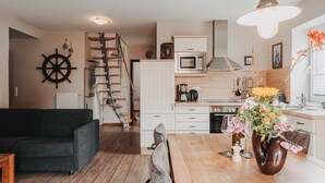 A modern kitchen with a wooden staircase, a dining area with a vase of flowers, and a black sofa. - Apartment 'Gorch Fock' with Shared Terrace, Shared Garden and Wi-Fi (Baltrum)