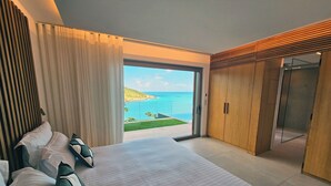 Een slaapkamer met een groot bed, een kledingkast en een glazen schuifdeur naar een balkon met uitzicht op zee.