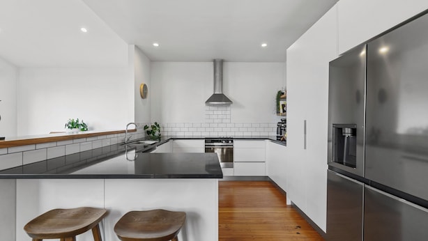 A modern kitchen with white cabinets, a stainless steel refrigerator, a built-in oven, and a wooden floor.