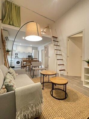 A modern living room with a sofa, two small tables, a hanging lamp, and a staircase leading to a kitchen area. - Nice apartment in Madrid neighborhood (Madrid)