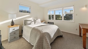 A bedroom with a bed, a nightstand, a lamp, a window, and a view of the outside. - Waterside Bliss - Taupo Holiday Home (Taupo)