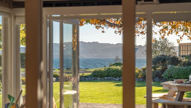 A patio area with a view of a lake and distant hills. - Waterside Bliss - Taupo Holiday Home (Taupo)