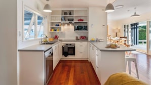 A modern kitchen with white cabinetry, a central island, and built-in appliances. - Waterside Bliss - Taupo Holiday Home (Taupo)