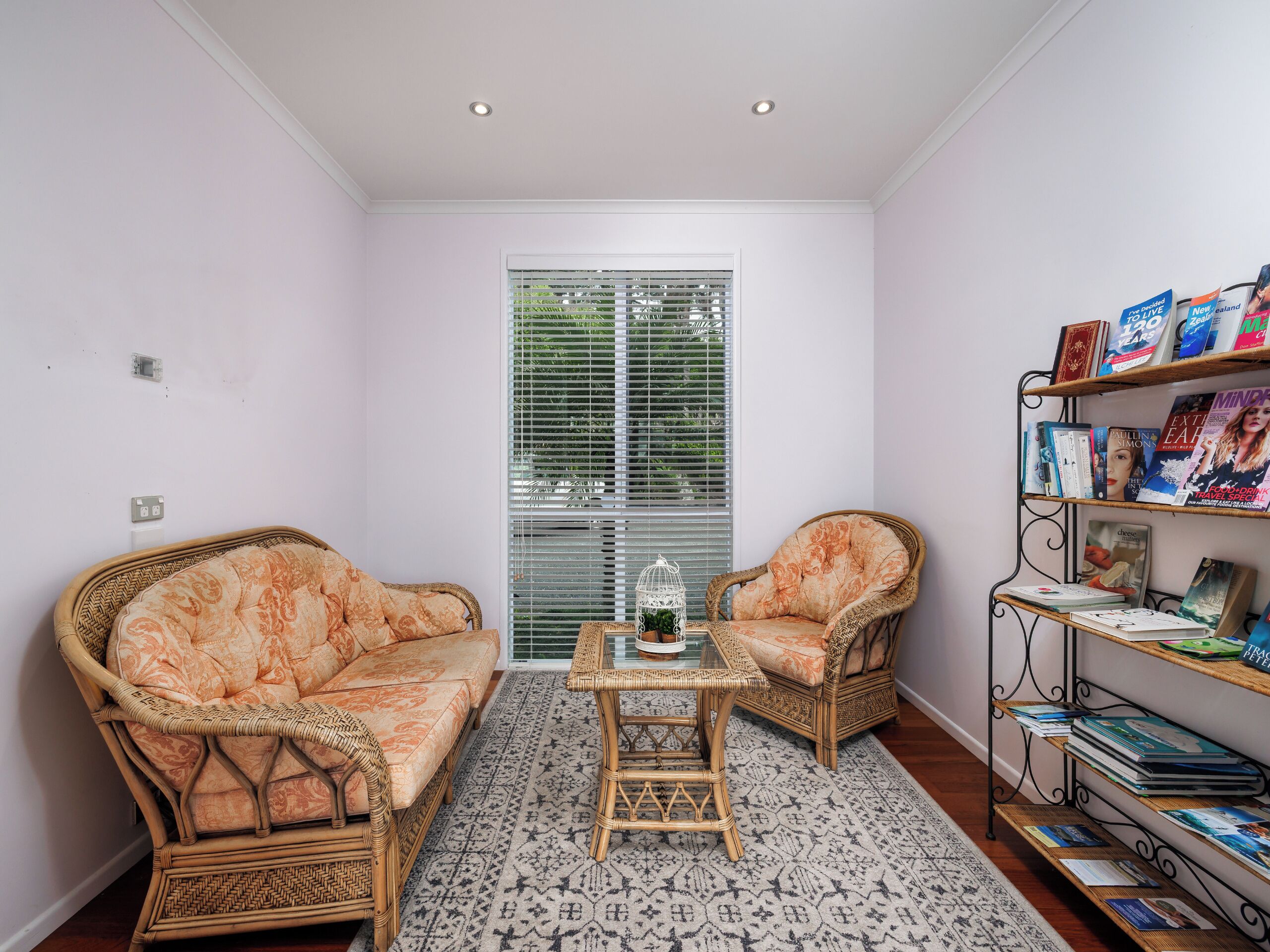 A cozy reading nook with wicker furniture, a small table, and a bookshelf filled with books.