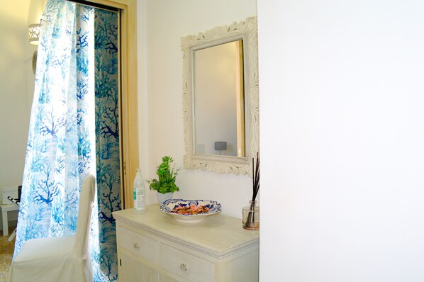 A bathroom with a white vanity, a mirror, a bowl of fruit, a potted plant, and a shower curtain with a blue tree pattern. - Lost in Amalfi, Your home in the heart of a peaceful village on the Amalfi Coast (Amalfi)