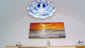 A room with a wall-mounted painting of a sunset over the ocean, a decorative ceiling light, and a wooden cabinet below. - Lost in Amalfi, Your home in the heart of a peaceful village on the Amalfi Coast (Amalfi)