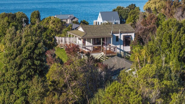 A coastal house with a large deck, surrounded by dense greenery and overlooking the sea.