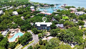 Luftaufnahme eines Küstenresorts mit einem zentralen Gebäude, umgeben von üppiger Vegetation, einer Marina mit Booten und einem Poolbereich.
