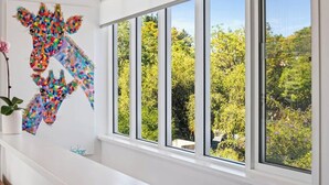 A room with a large window, a colorful giraffe artwork on the wall, and a potted plant.