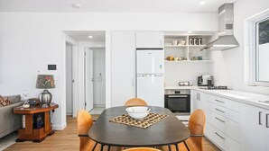 A modern kitchen with white cabinets, a built-in oven, and a microwave. There is a dining table with chairs and a bowl on it.