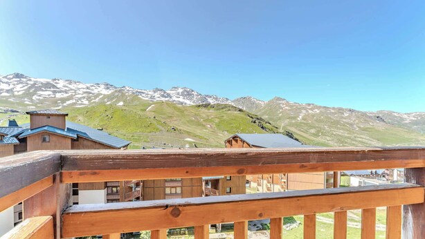 Un balcon en bois offrant une vue sur des montagnes enneigées et un ciel dégagé.