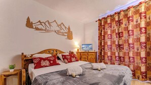 A bedroom with a bed, wooden headboard, decorative wall art, a television, and a curtain with a patterned design.