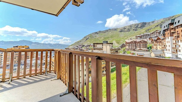 A balcony with a wooden railing overlooking a mountainous area with buildings.