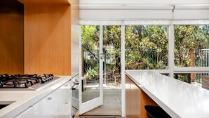 Eine moderne Küche mit Gaskochfeld, weißen Schränken und Blick auf einen Garten durch große Fenster.
