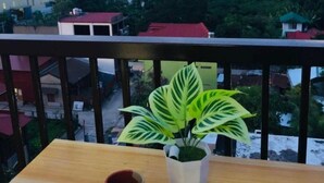 Een balkon met een houten tafel, een plant in pot en een rode mok.