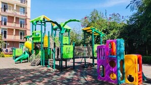 Een speeltuin met kleurrijke speeltoestellen en een gebouw op de achtergrond.