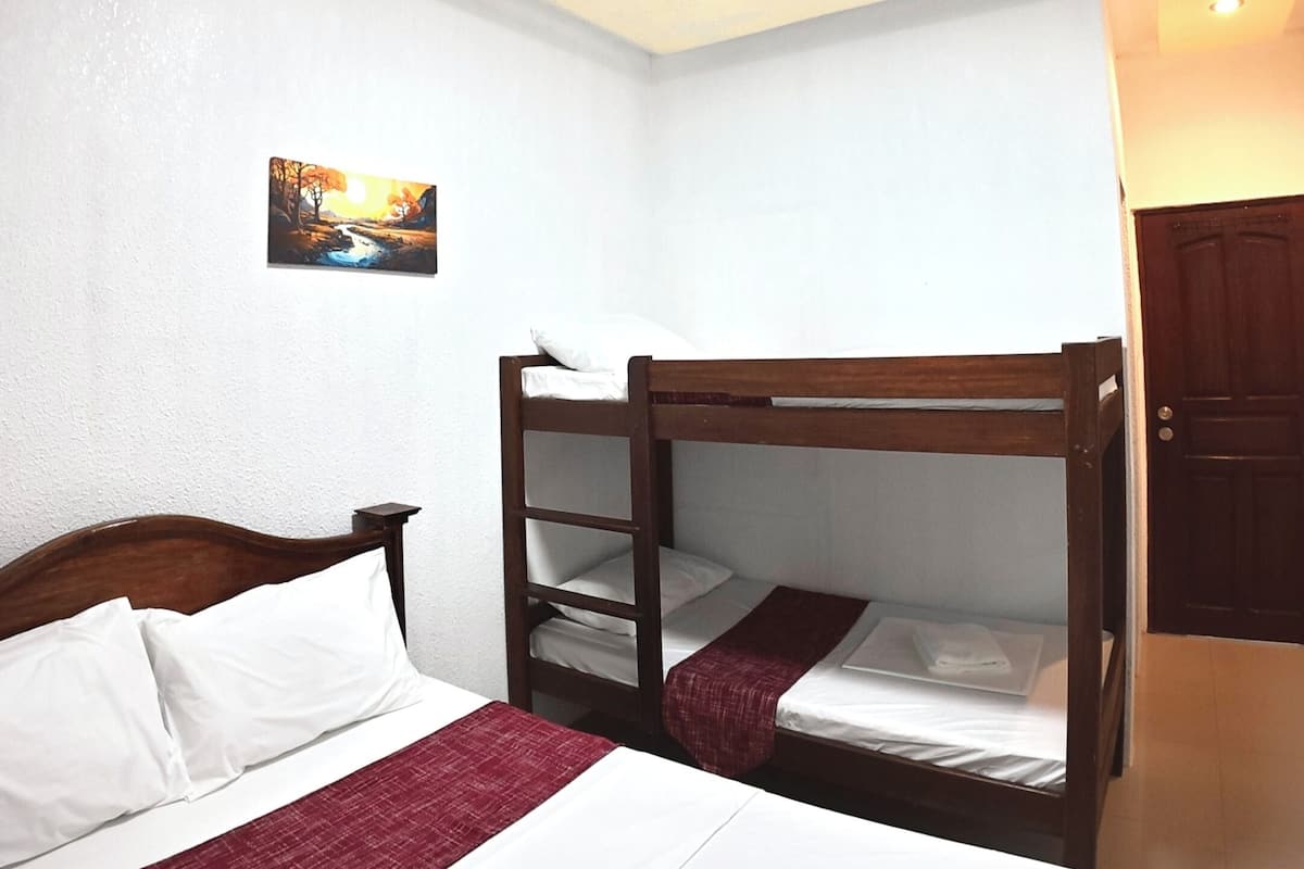 Una habitación de hotel con una litera, una cama individual, un cuadro en la pared y una lámpara en el techo.