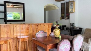 A dining area with a wooden table and chairs, a bar counter, and a television mounted on the wall. - Cozy Stop Inn (Puerto Princesa)