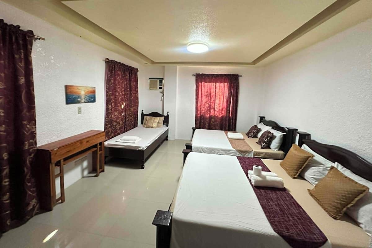 Una habitación de hotel con dos camas individuales, un escritorio, una silla, un banco, un cuadro en la pared y una ventana con cortinas.