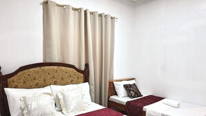 A hotel room with two beds, a headboard with floral pattern, a ceiling light, and a window with curtains. - Cozy Stop Inn (Puerto Princesa)