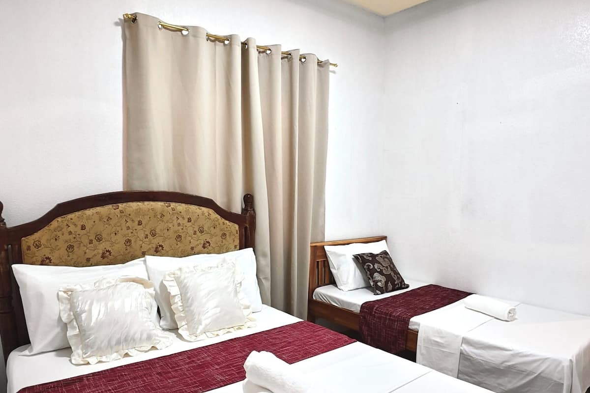 Habitación de hotel con dos camas, cabecera con estampado floral, una lámpara de techo y una ventana con cortinas.
