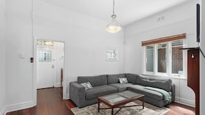 A living room with a sectional sofa, a glass coffee table, and a wooden floor.