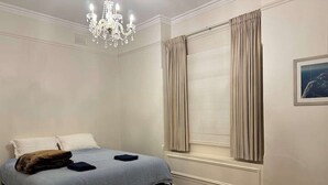 Une chambre à coucher avec un lit, un lustre, une fenêtre avec des rideaux et un tableau au mur.