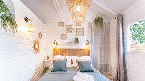 Une chambre à coucher bien rangée, avec un lit, des oreillers, une table de chevet et une plante suspendue.
