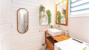 Une salle de bain avec un meuble-lavabo blanc, un miroir et des plantes suspendues.