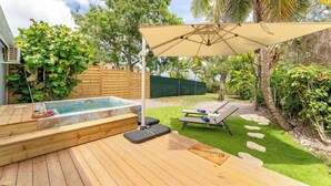 Une terrasse en bois avec un jacuzzi, des chaises longues et une pergola offrant de l’ombre.