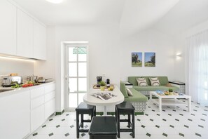 A modern kitchen with white cabinets, a dining table with two black stools, a green sofa, and a coffee table. - Campo Golf 68 by VillaGranCanaria (Las Palmas de Gran Canaria)