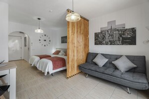 Une chambre à coucher moderne avec un lit, un canapé gris, une cloison en bois, un tableau représentant un paysage urbain et une horloge murale.