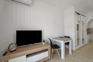 Una sala de estar moderna con un televisor de pantalla plana, una mesa de centro de madera, una silla negra y una pequeña planta en maceta.