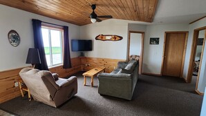 A cozy room with a wooden ceiling, a flat-screen TV, a sofa, a recliner, and a small table. - 3-bedroom Cabin at West Wind Resort in beautiful Waskish, MN on Upper Red Lake. (Waskish)
