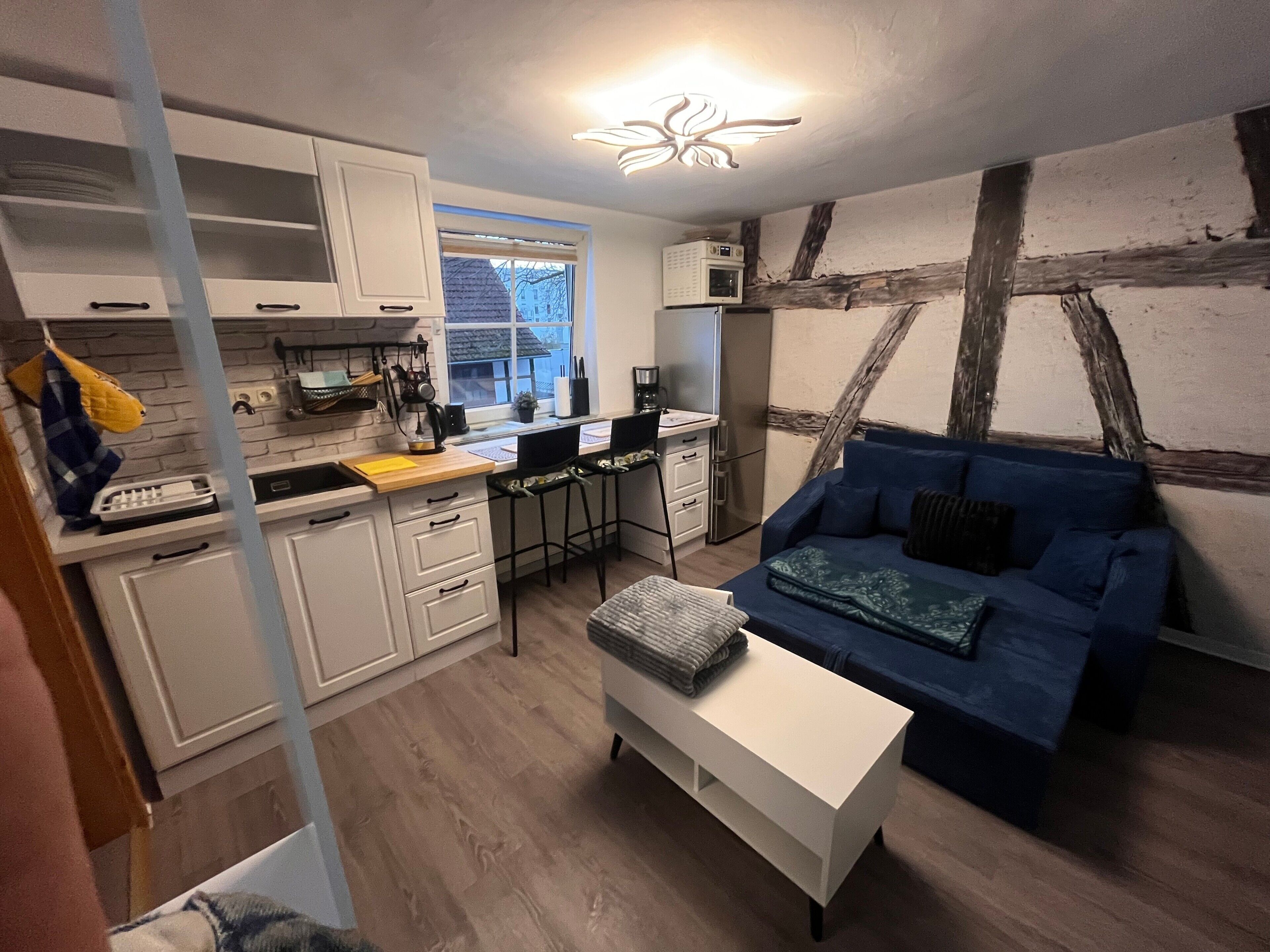A compact living space with a kitchenette, a blue sofa, a white coffee table, and a ceiling light fixture.