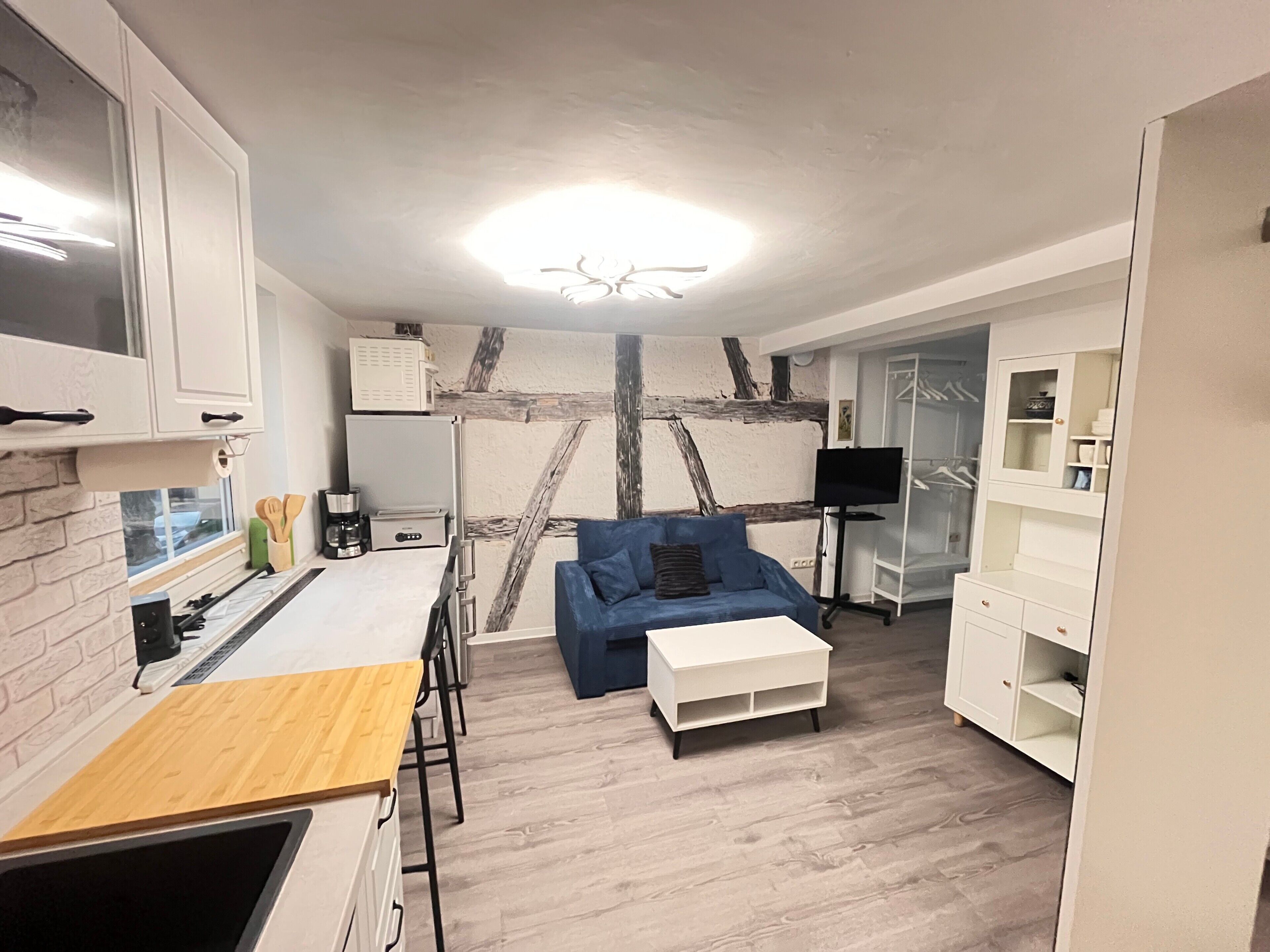 Een moderne woonkamer met een blauwe bank, een witte salontafel en een keukenhoek met een metselwerk accentmuur.