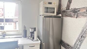 Una cocina compacta con un refrigerador de acero inoxidable, un microondas arriba, una cafetera y una ventana con vista a edificios.